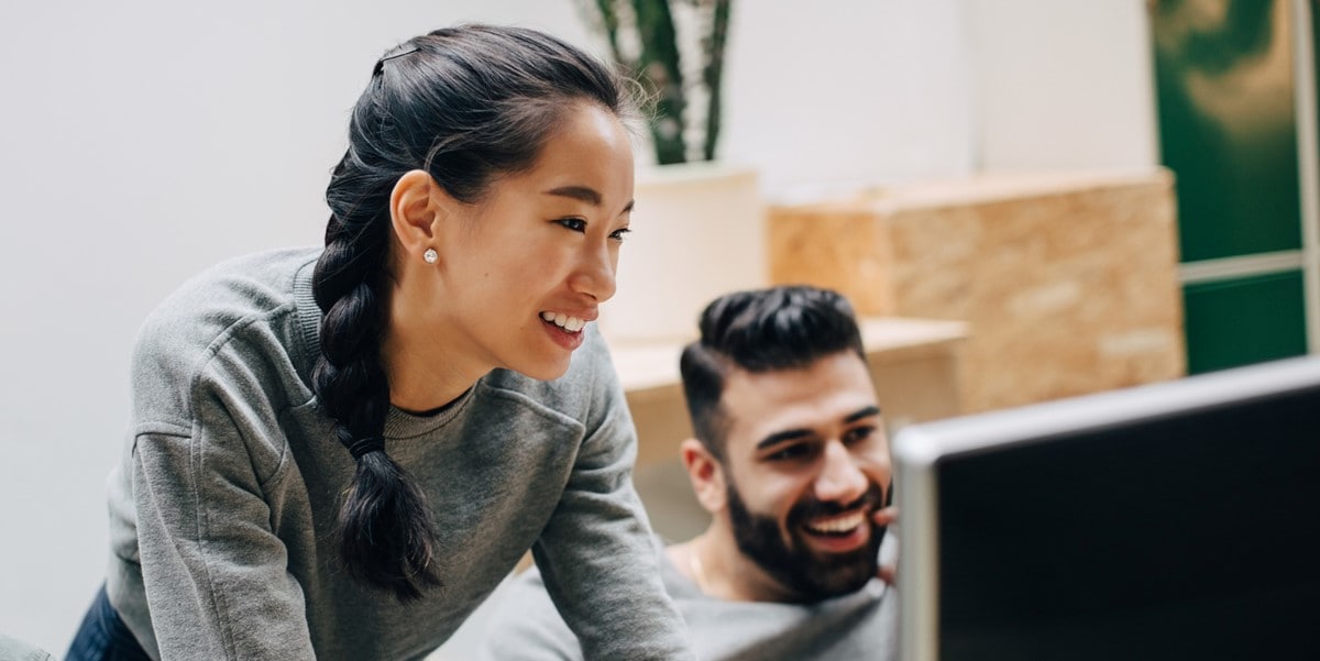 two people at a desk looking at computer