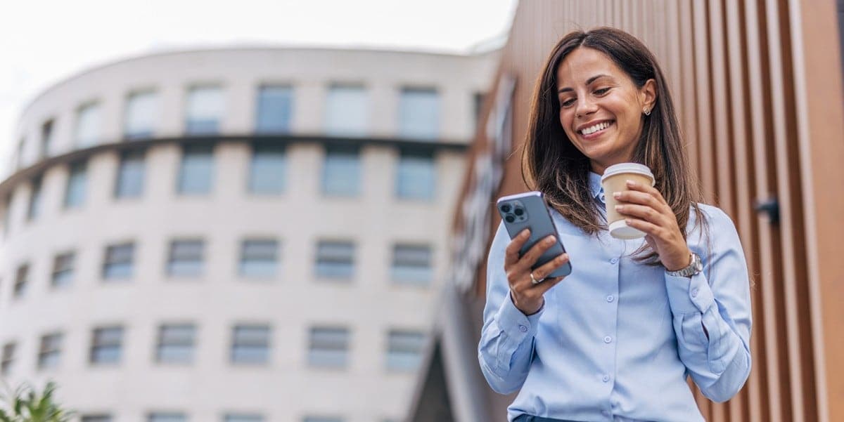 travler outside building holding coffee cup, looking at cellphone